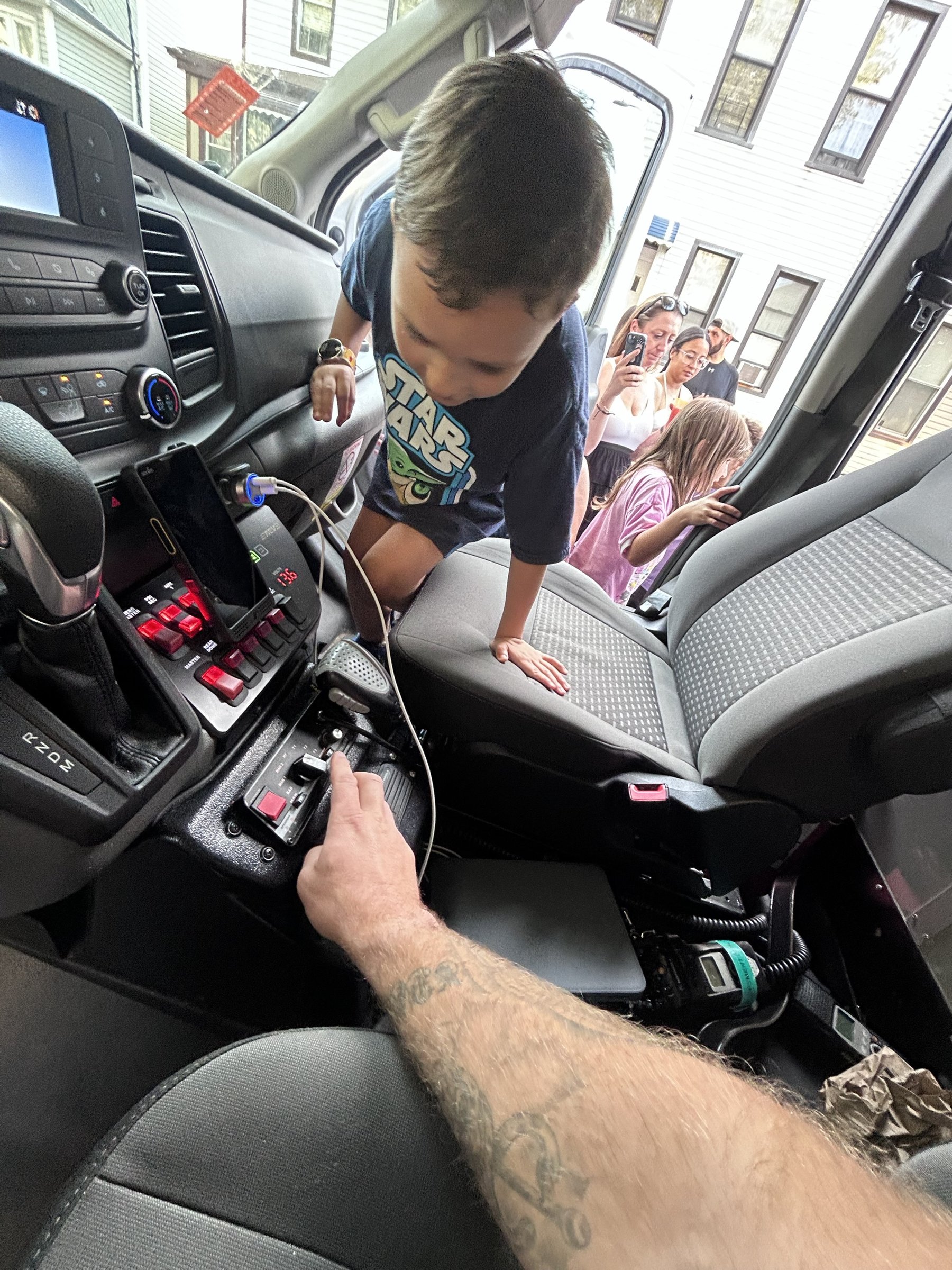 A small child standing at the front console of the ambulance while a crew member points out the switches and controls