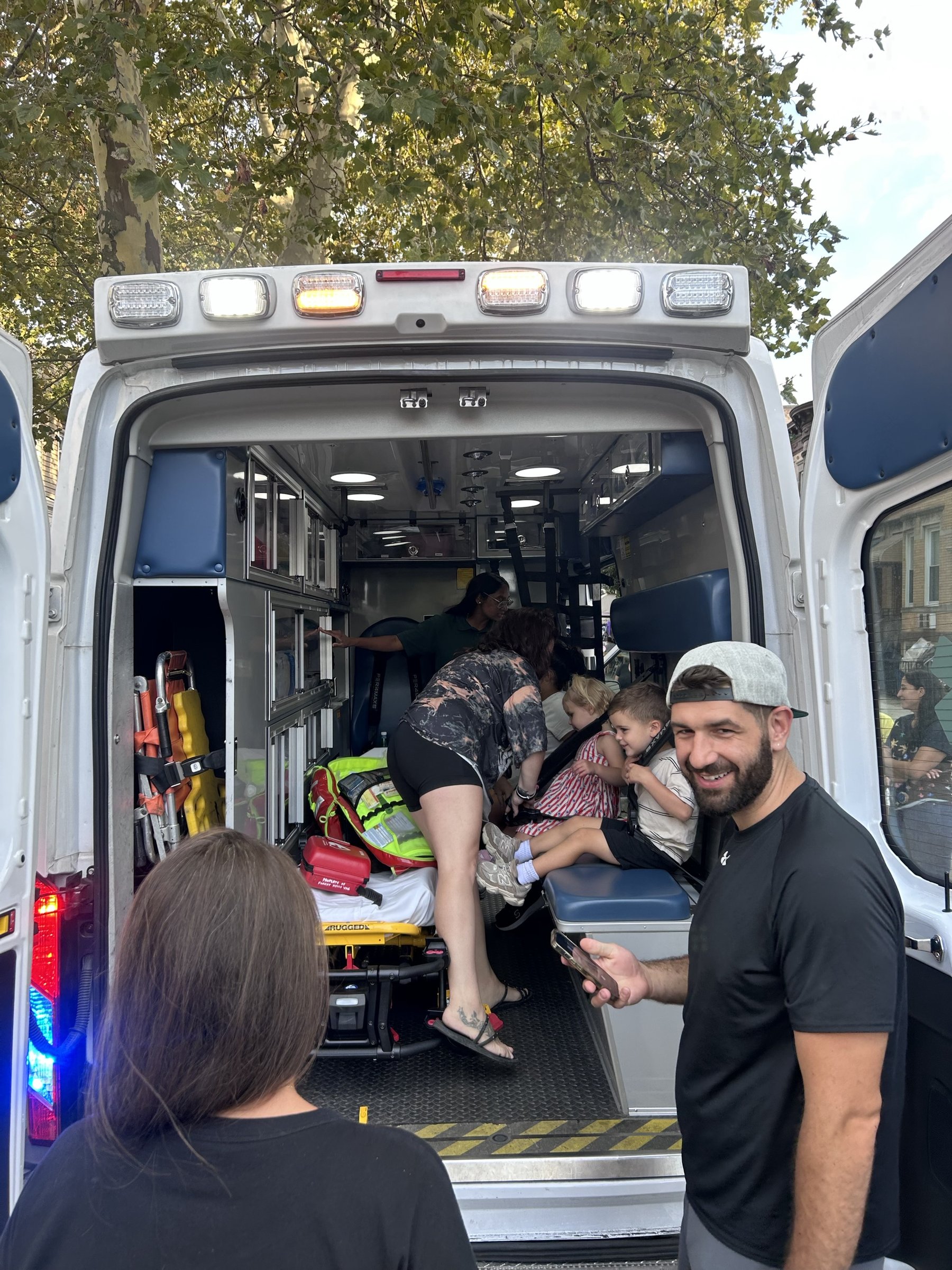Children sitting on the bench seat inside the back of ambulance FH4 while a parent helps them up