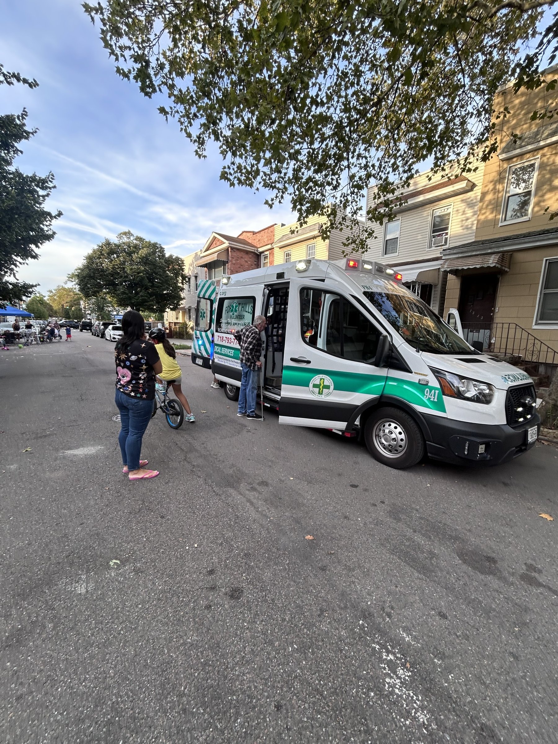 FHVAC ambulance FH4 parked along a tree-lined residential street, side door open, with block party tents visible down the road